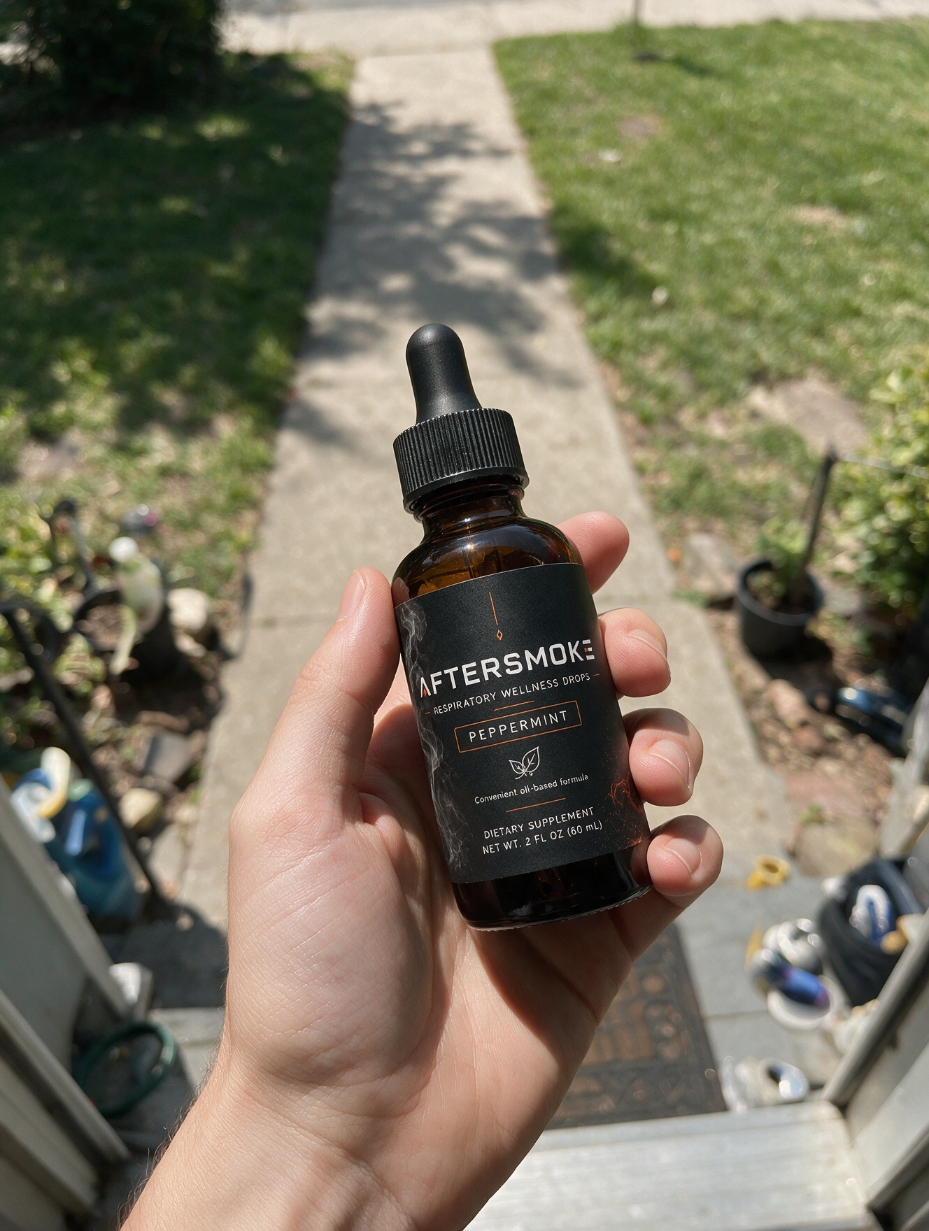 AfterSmoke bottle held in hand outside on a sunny sidewalk
