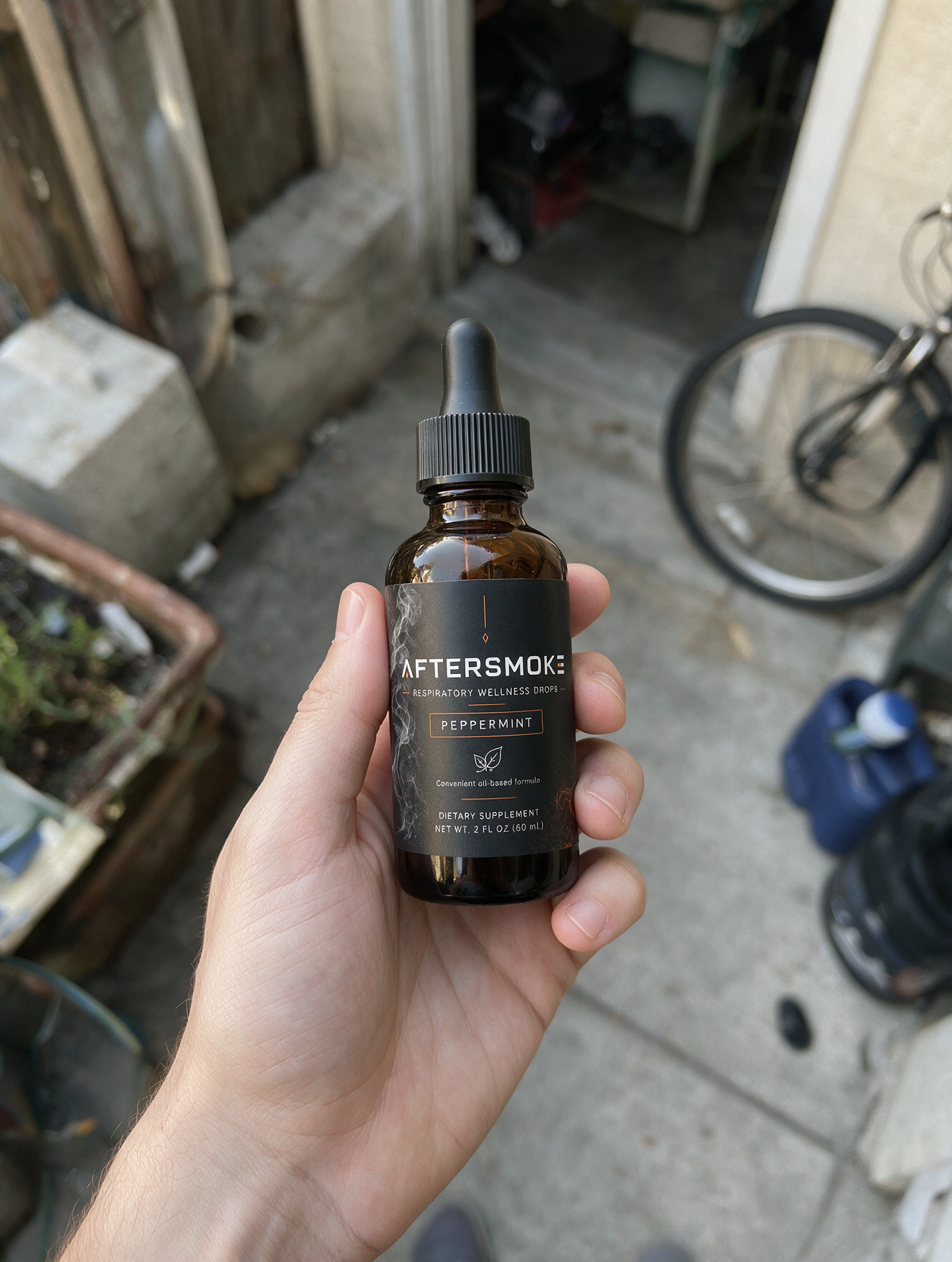 AfterSmoke bottle held in hand in a sunny side yard
