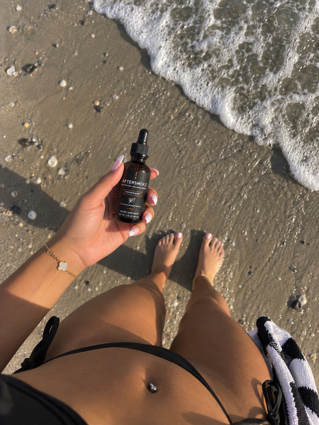AfterSmoke bottle held in hand at the water's edge on the beach