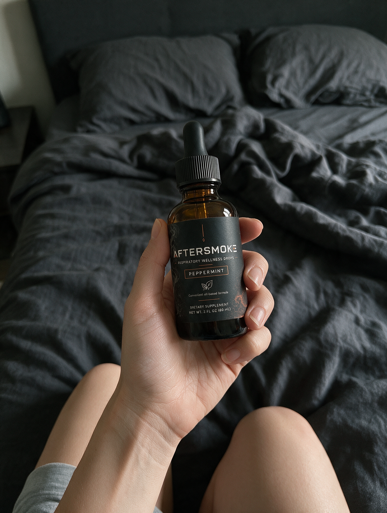 AfterSmoke bottle held in hand over dark bedding