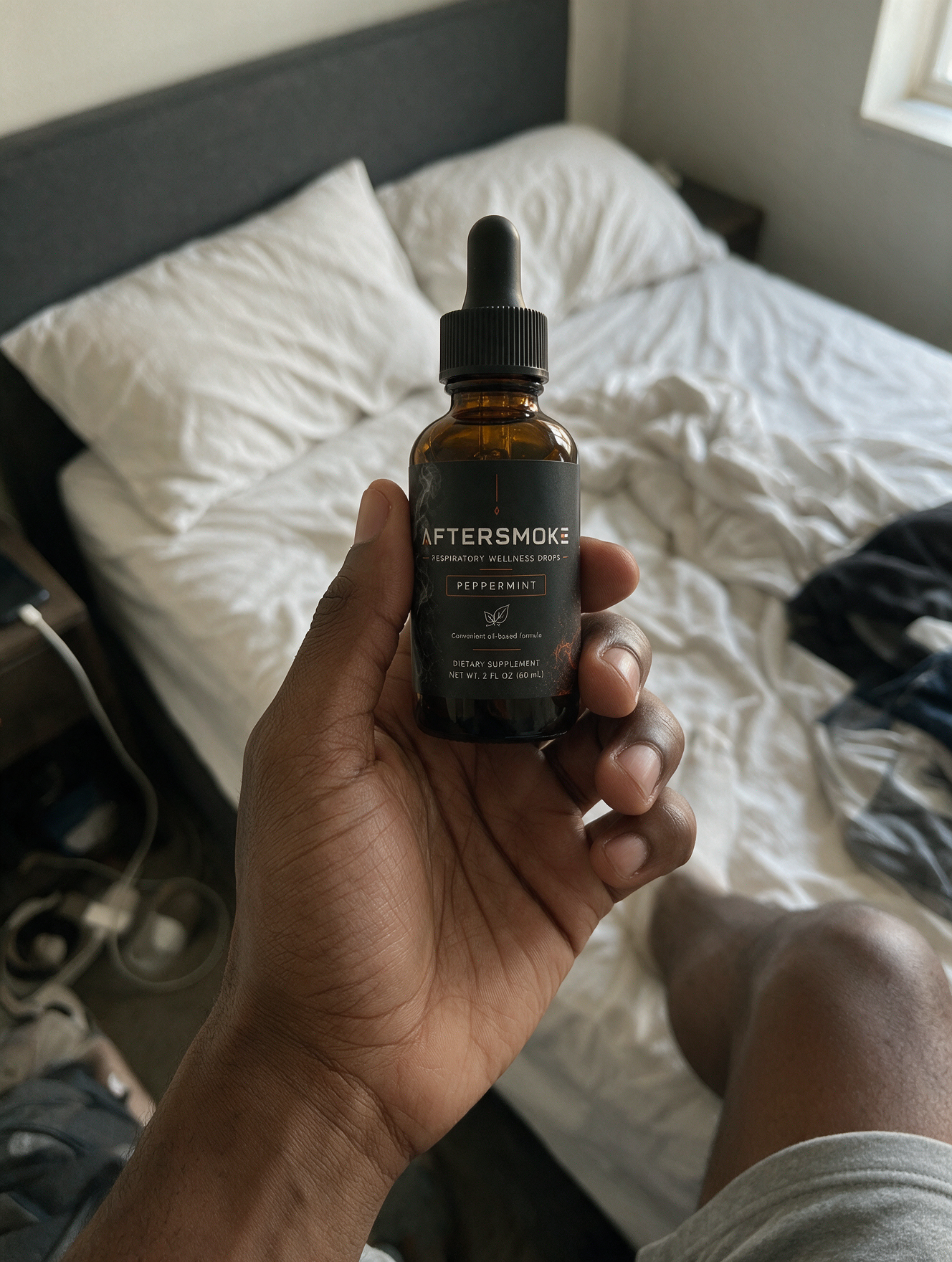 AfterSmoke bottle held in hand over an unmade bed