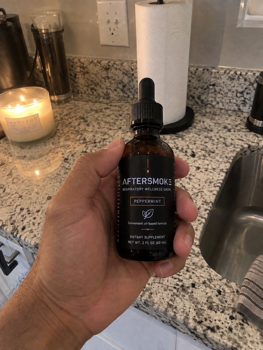 AfterSmoke bottle held in hand by the kitchen sink
