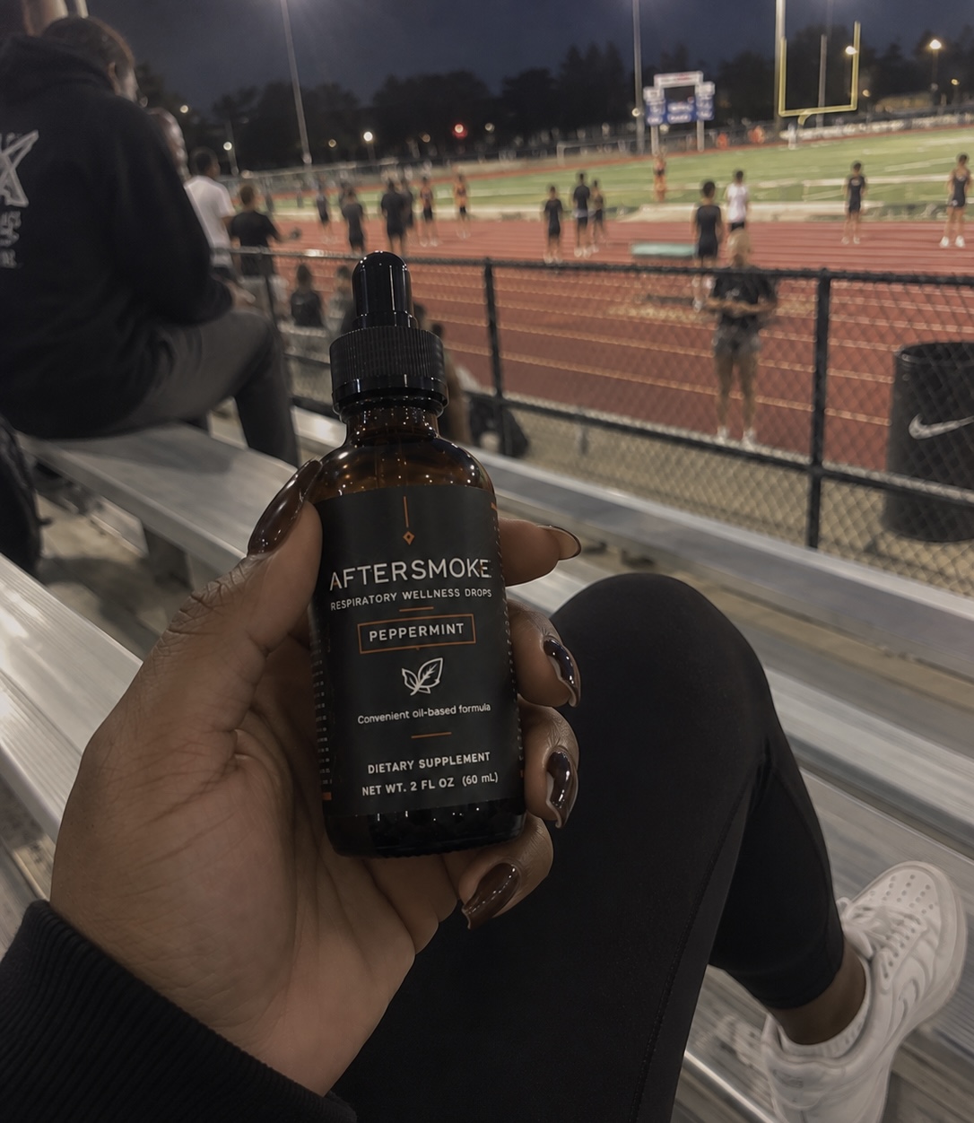AfterSmoke bottle held in hand in the bleachers at a running track